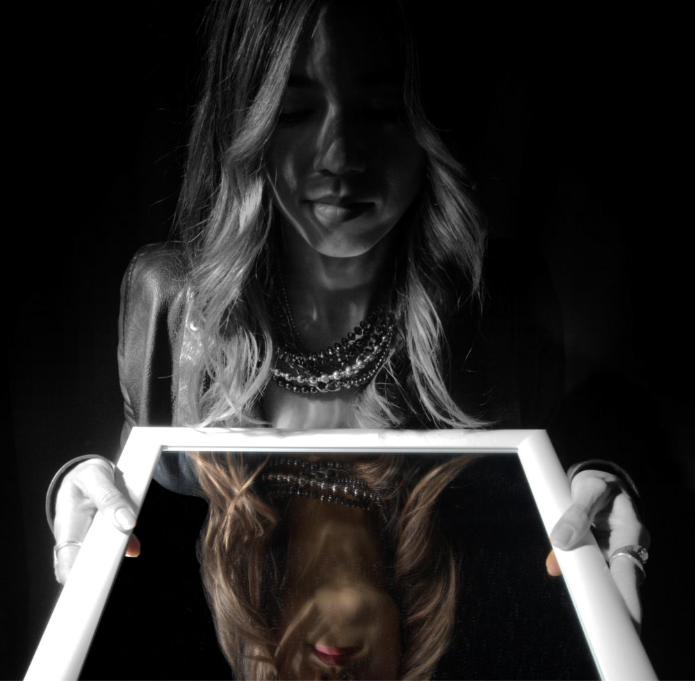 A creative portrait of a young lady looking into a mirror. Her reflection is in colour while she is black and white