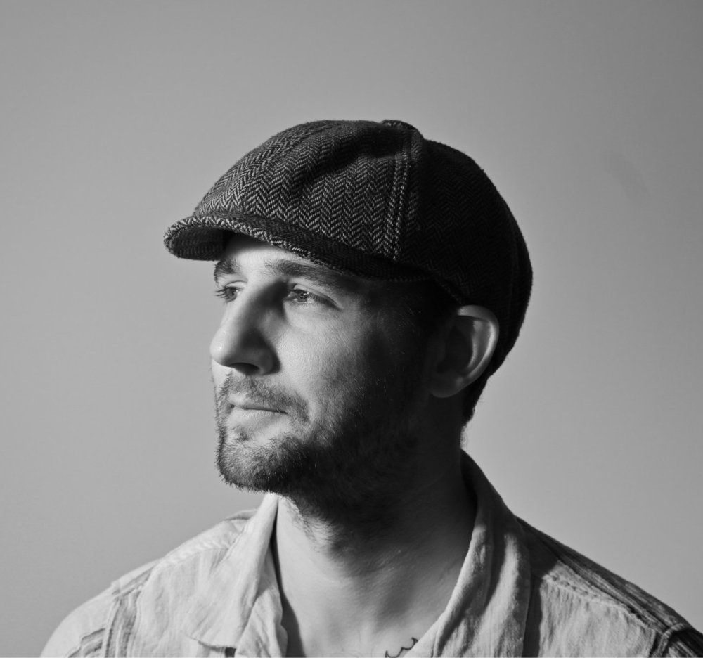 A black and white portrait photograph of a young man wearing a hat looking into the distance